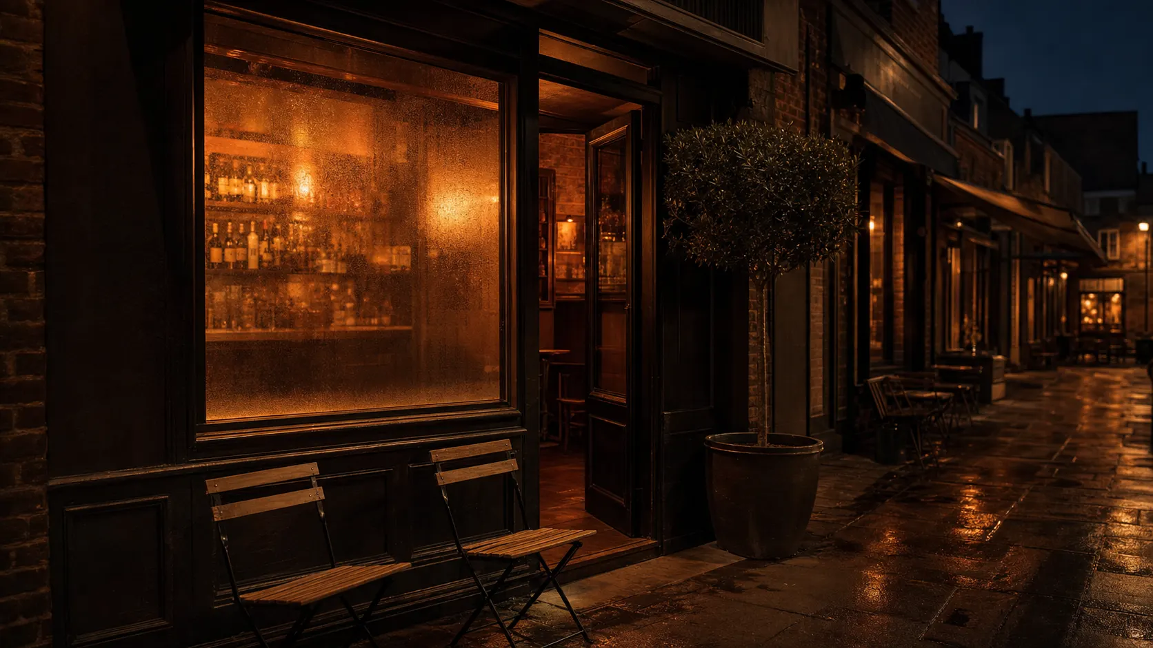 A dim bar-district street at dusk, storefront windows glowing warm.