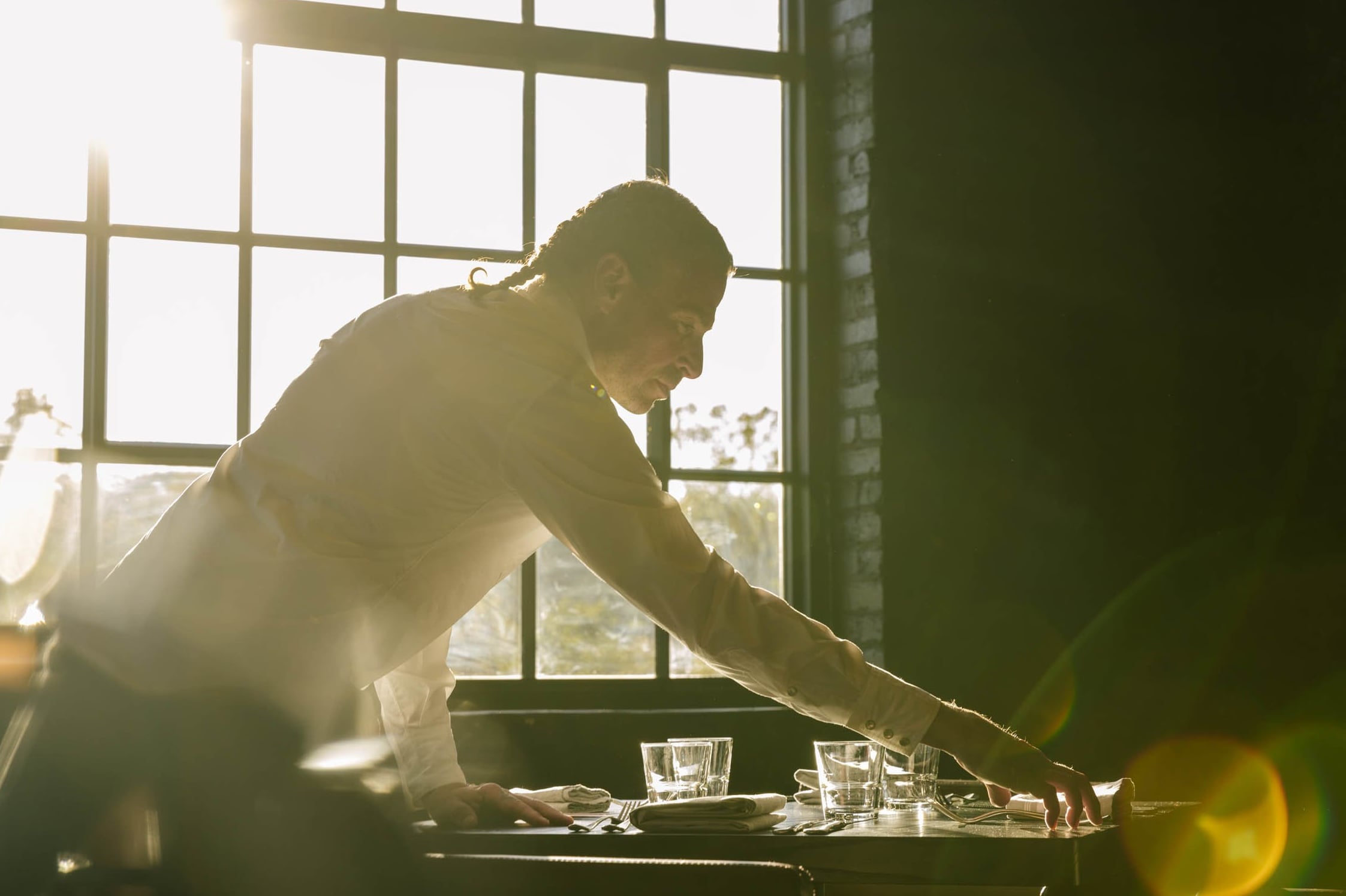 Server setting the table bathed in golden afternoon light through industrial windows.