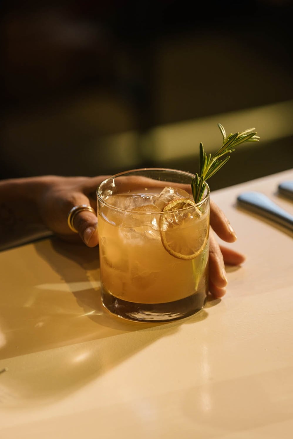 Handcrafted cocktail with rosemary garnish and dried citrus on the warm-lit bar.