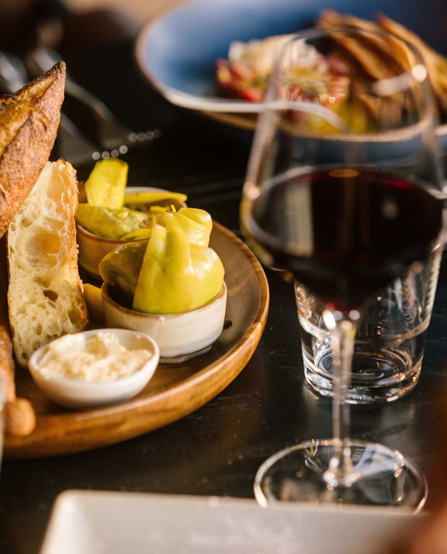 Platter with fresh baguette, pickled peppers, and tapenade with a glass of red wine.