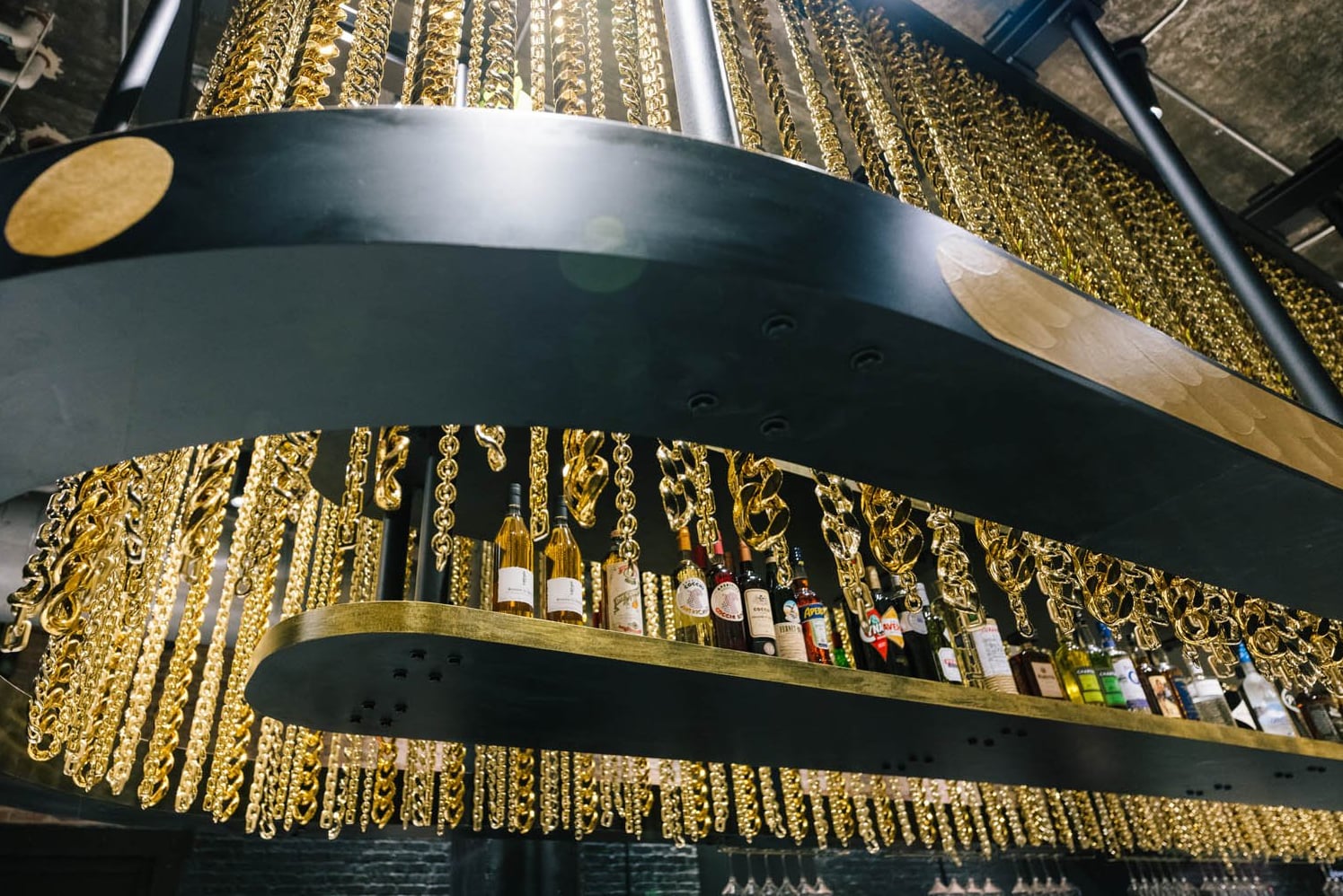 Dramatic backbar adorned with cascading gold chain curtain and curated spirit selection.