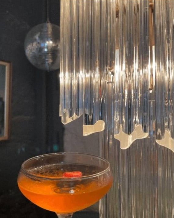 Orange cocktail beneath hanging glass decor