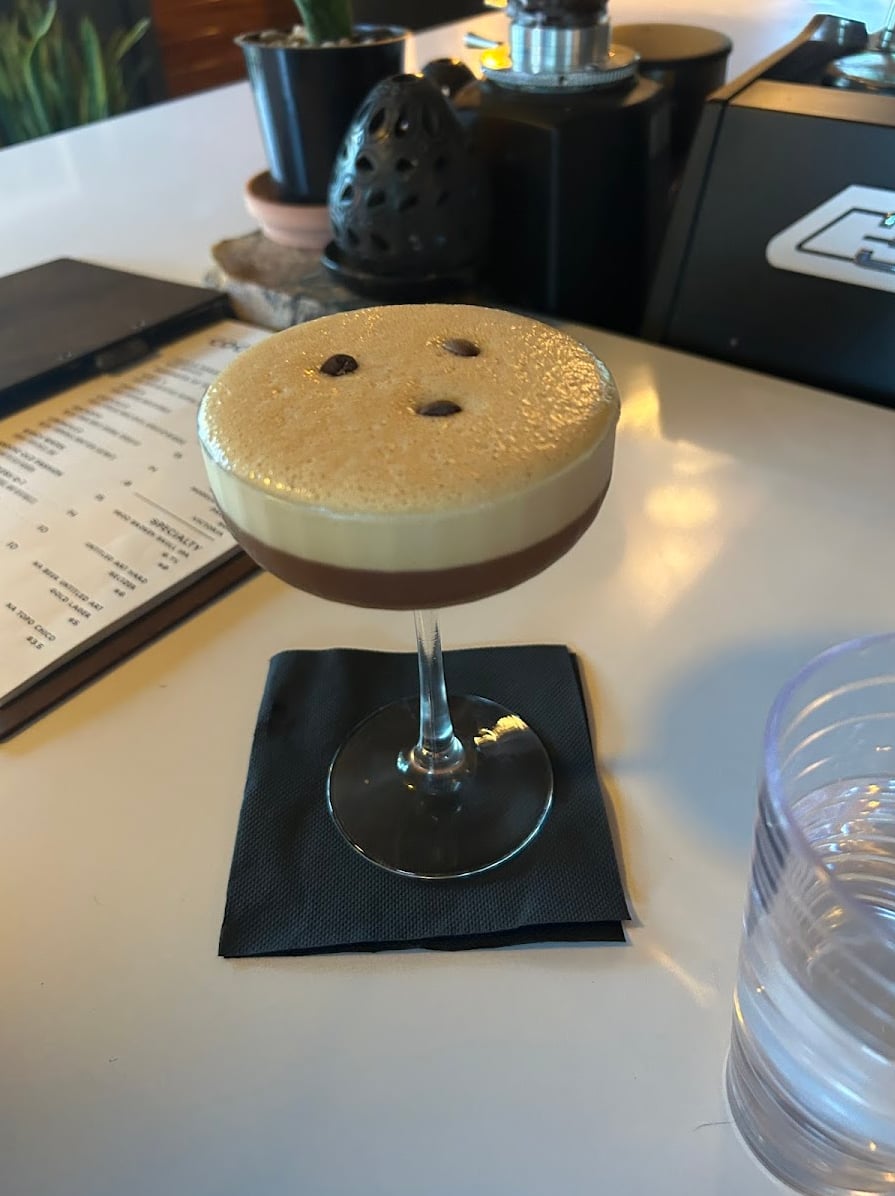Espresso martini-style coupe with a perfect foam cap served on the white bar counter