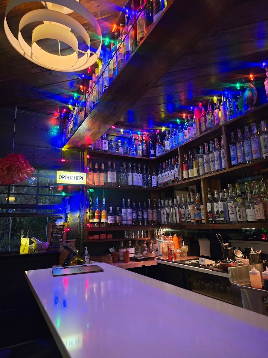 Full backbar lined with spirits under colorful ceiling lights and the signature white bar counter