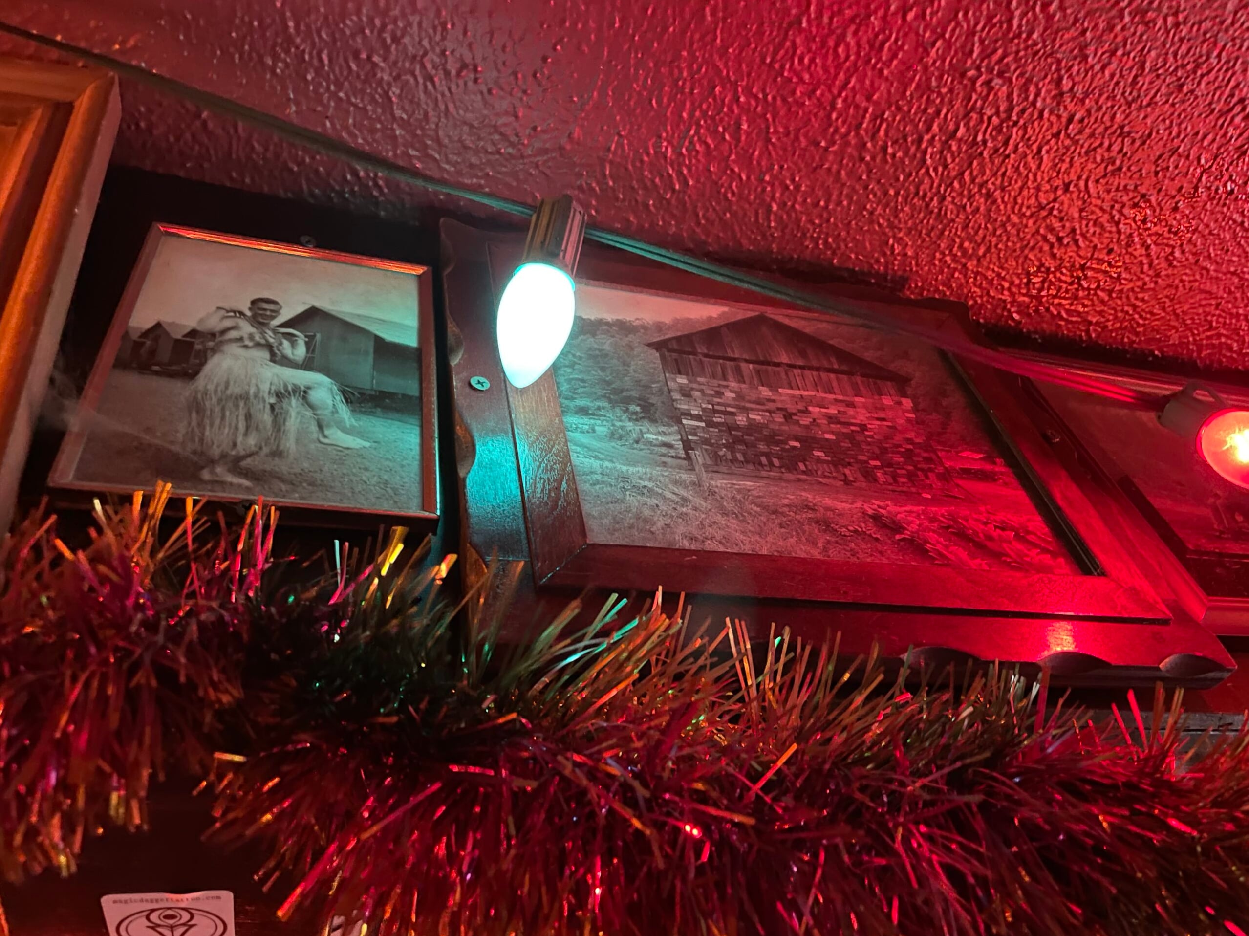 Vintage framed photos and tinsel garland adorn the red-lit ceiling walls — quintessential Double Crown eclectic decor