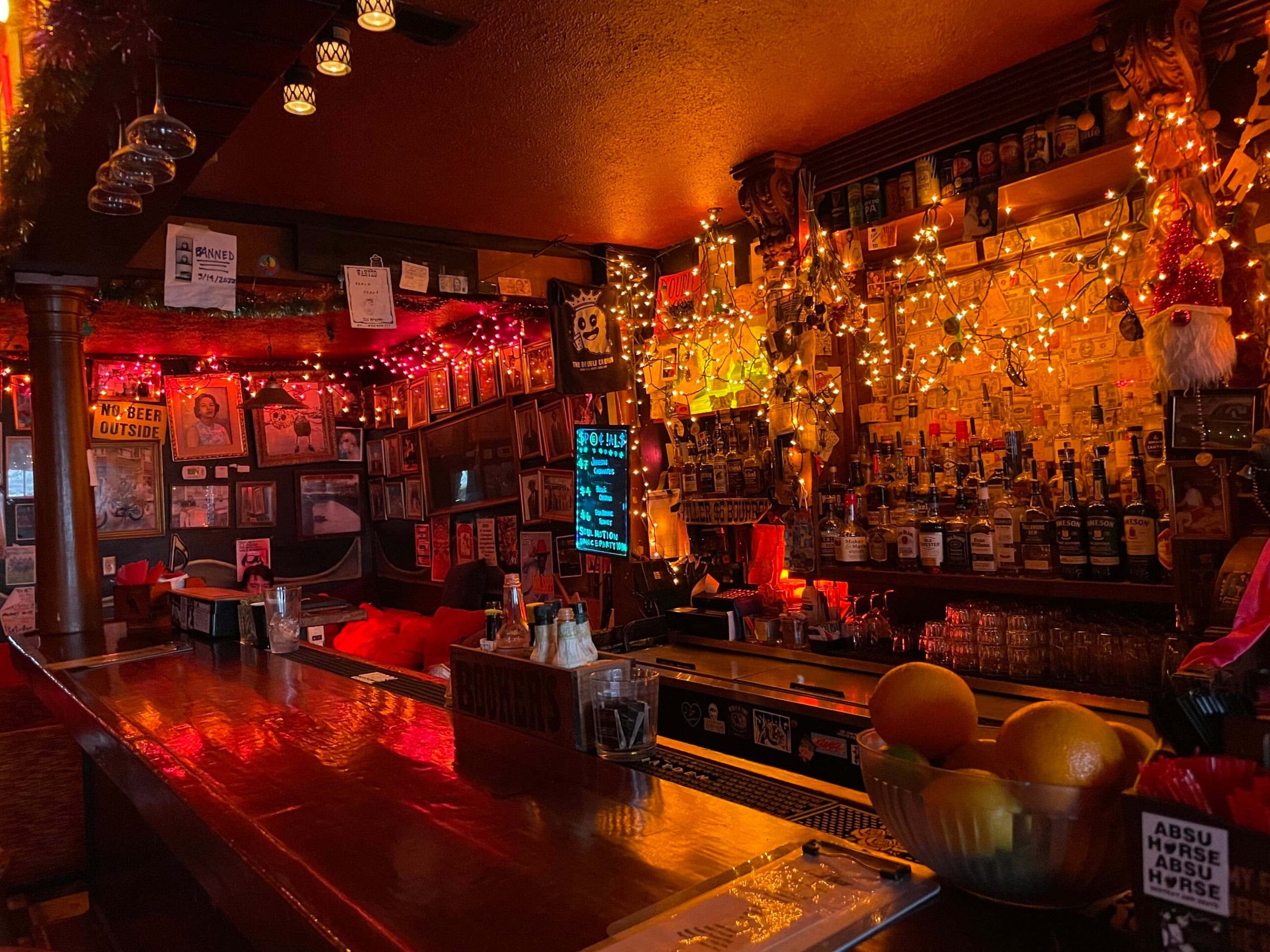 Bar counter looking down the length of the backbar, fully stocked with bottles and draped in warm twinkling lights