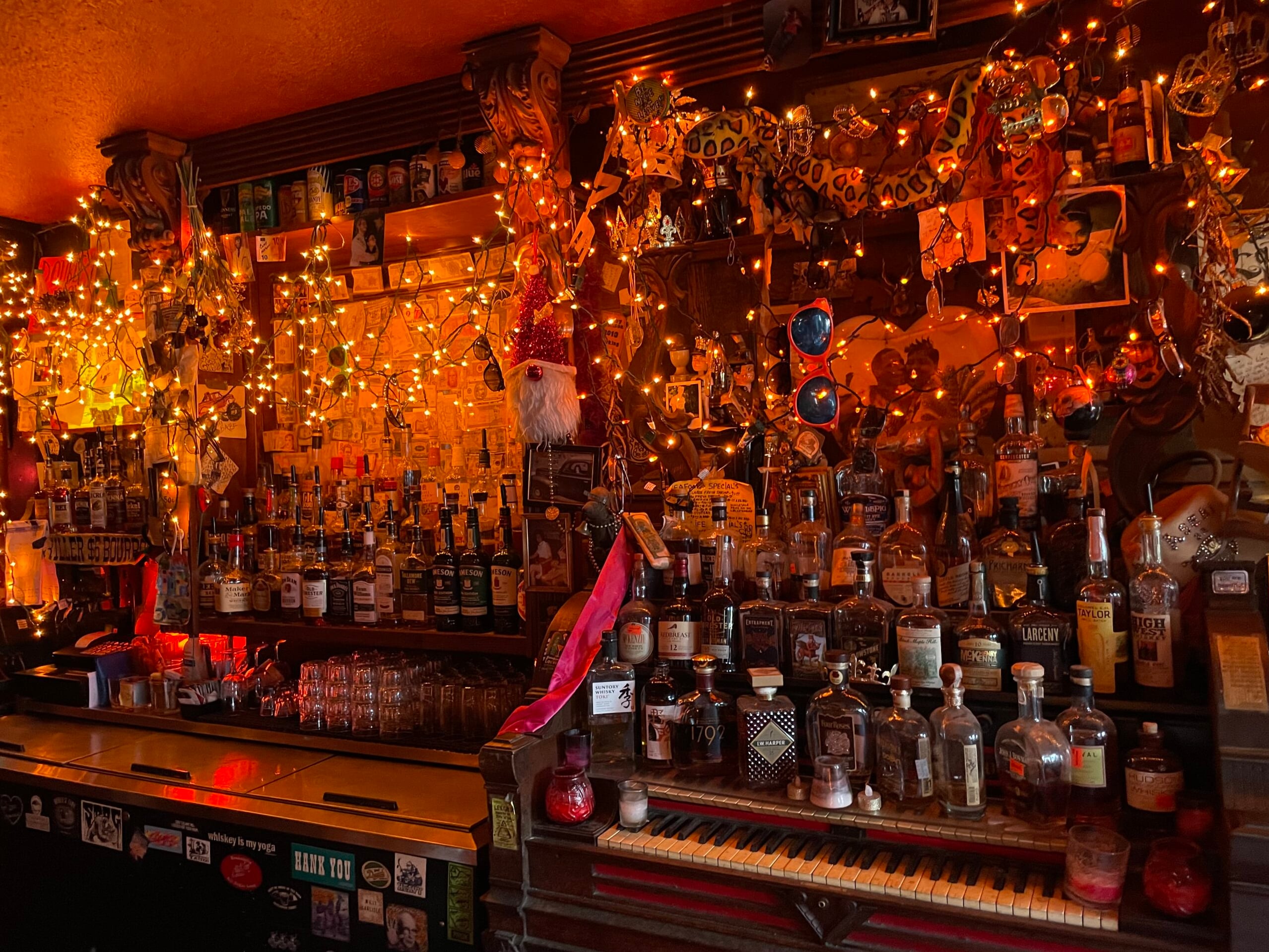 The legendary back bar — whiskey bottles lined along a vintage piano keyboard beneath layers of string lights and eclectic wall art