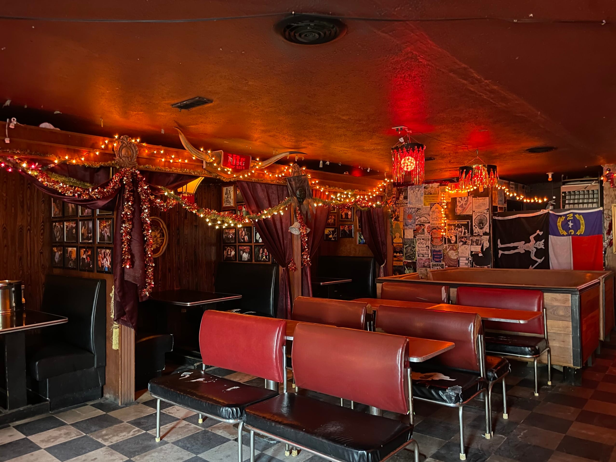 The intimate red-lit interior with christmas string lights, checkered tile floor, and leather booth seating