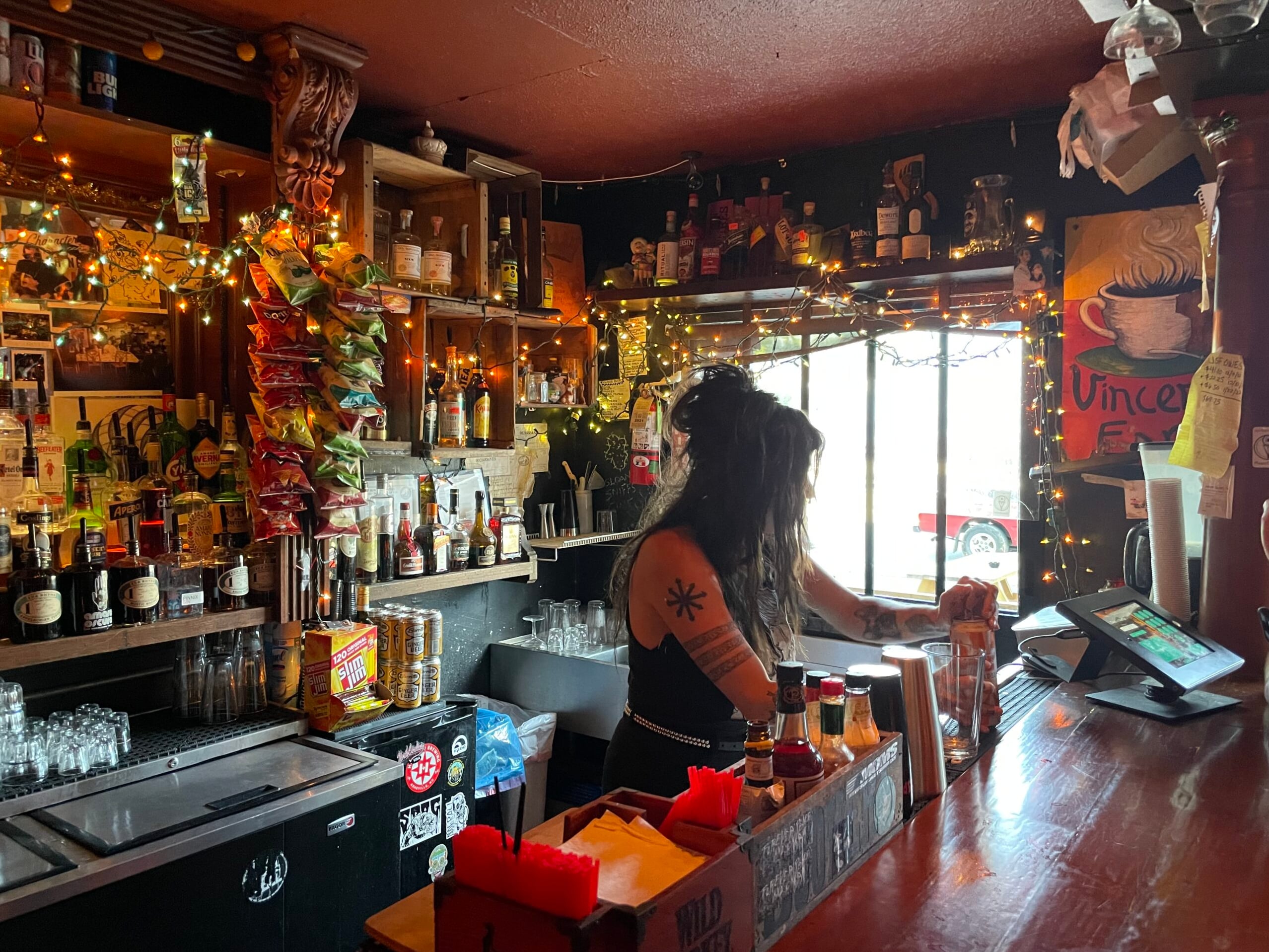 Bartender at work behind the eclectic, light-strewn bar counter