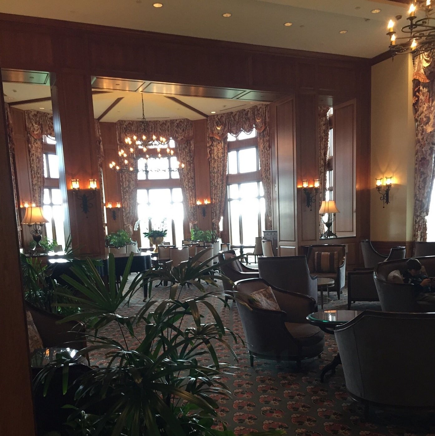 Warm, wood-paneled lounge with grand piano, chandelier, and cozy club chairs