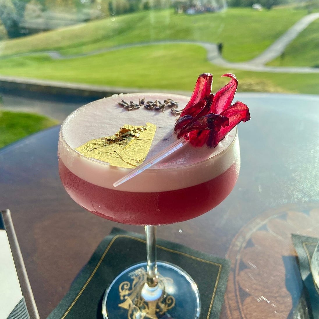 Signature craft cocktail finished with gold leaf and dried florals, overlooking the estate lawn