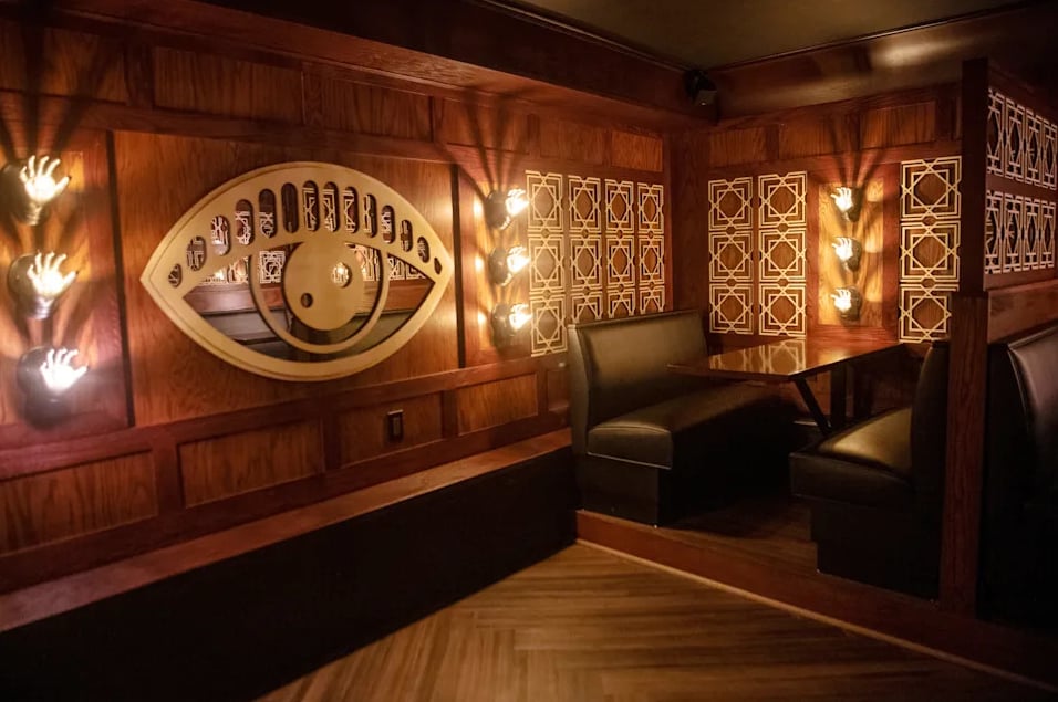 Eye mural on wood-paneled walls with golden hand wall sconces and leather booths