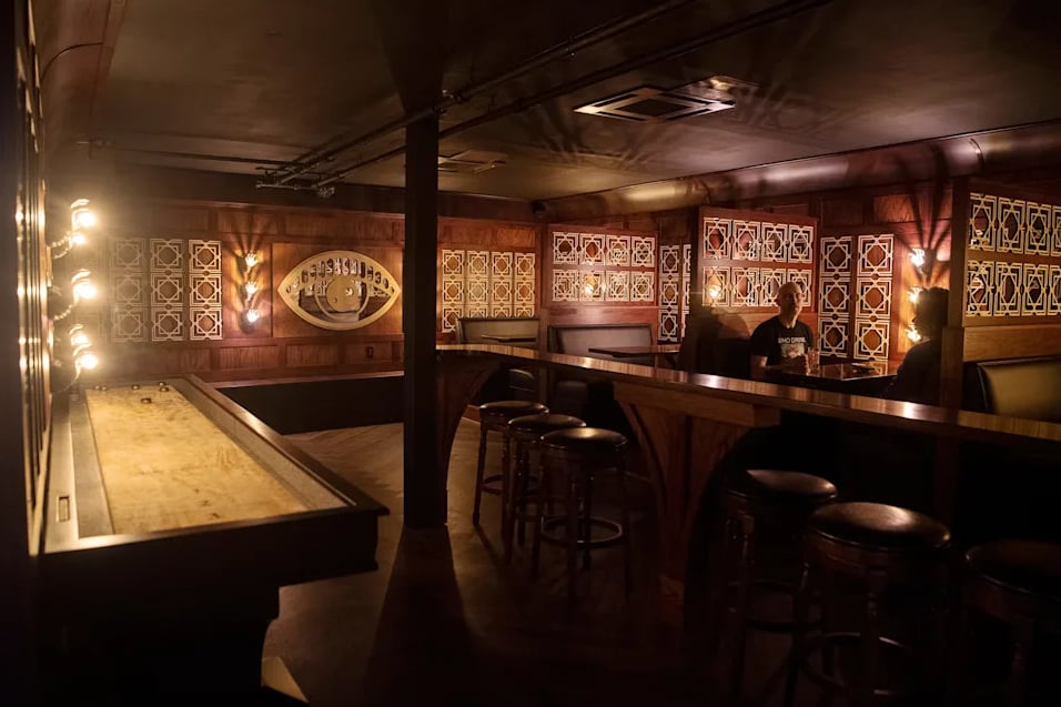 The full underground room: shuffleboard, bar stools, and warm amber lighting.