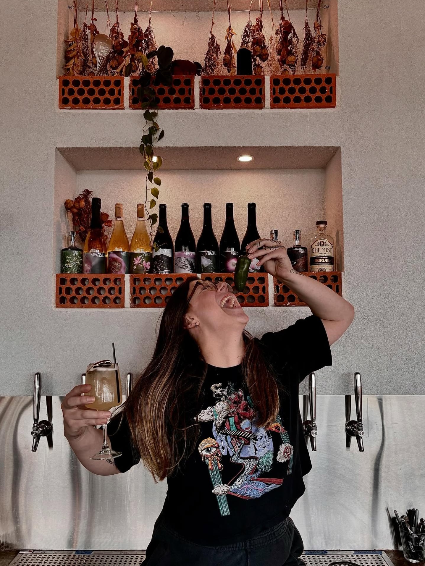 Playful bartender moment with rustic brick shelving featuring wine and spirits.