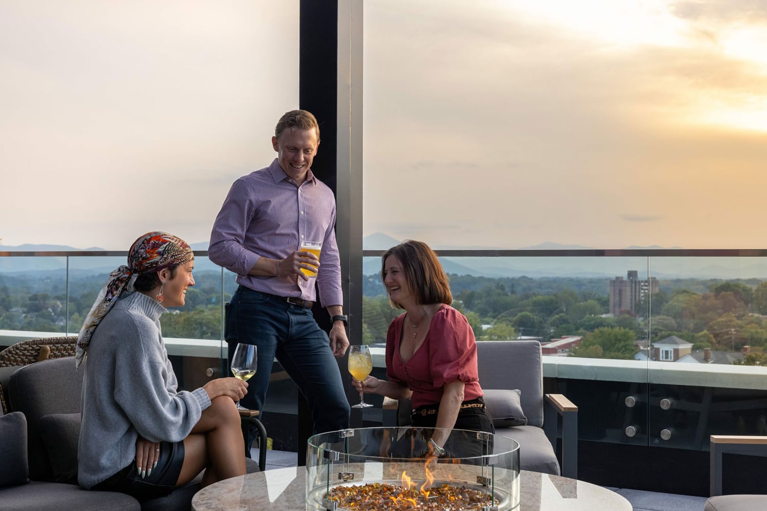 Rooftop patio guests enjoying drinks and conversation around a fire pit at sunset.