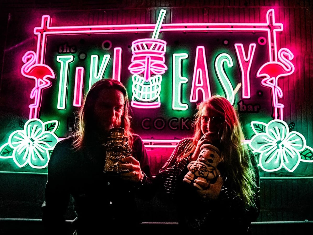 Vibrant neon Tiki Easy Bar sign with guests enjoying tropical cocktails