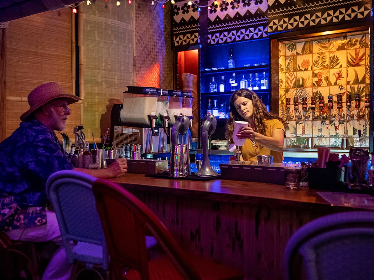 Bartender at work behind the tiki-themed bar with elaborate mural backbar