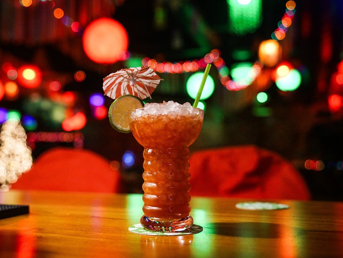 Signature tiki cocktail in a carved mug with paper umbrella and colorful bokeh lights