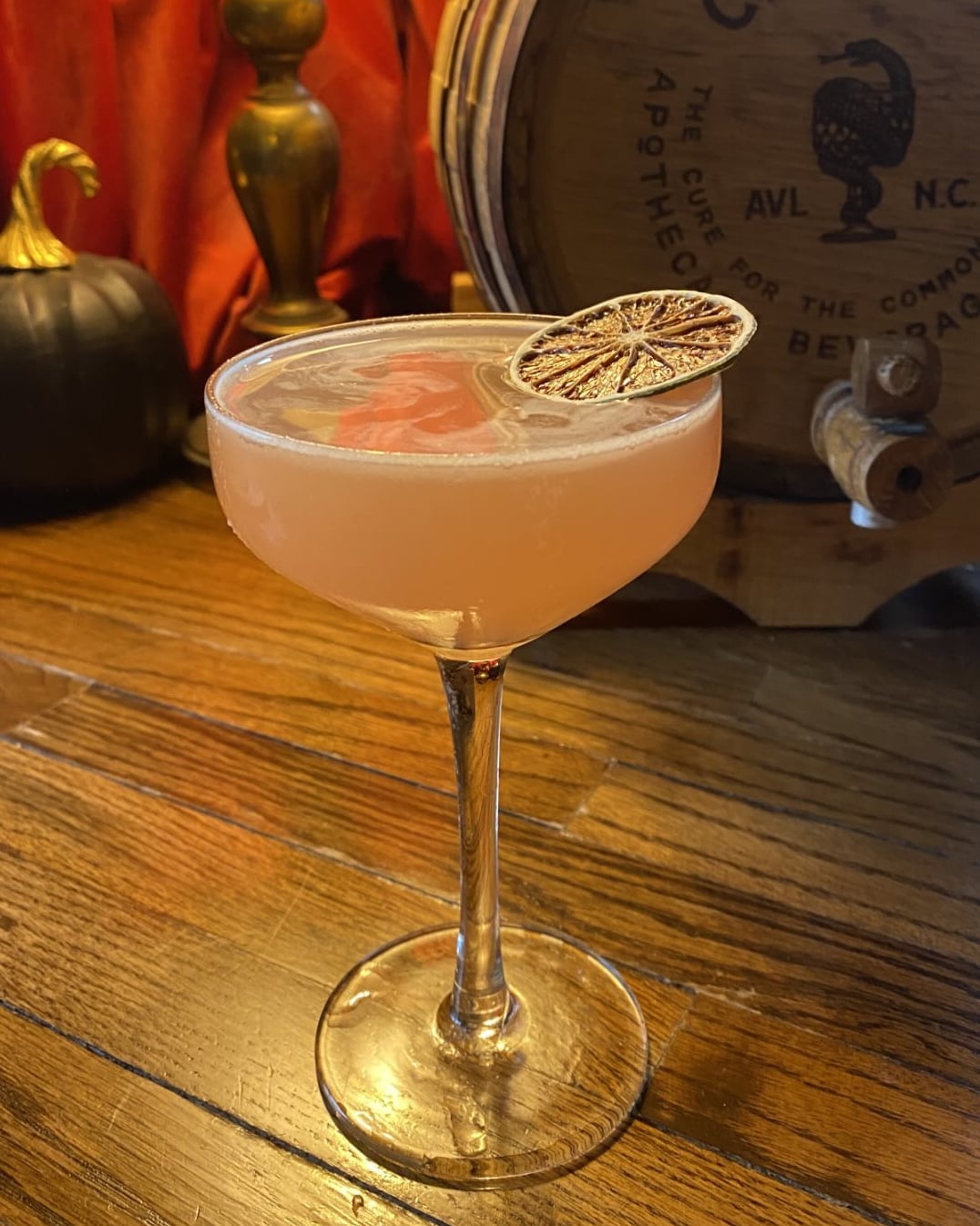 Pink cocktail featuring a smoked rose gold leaf garnish and dried citrus wheel.