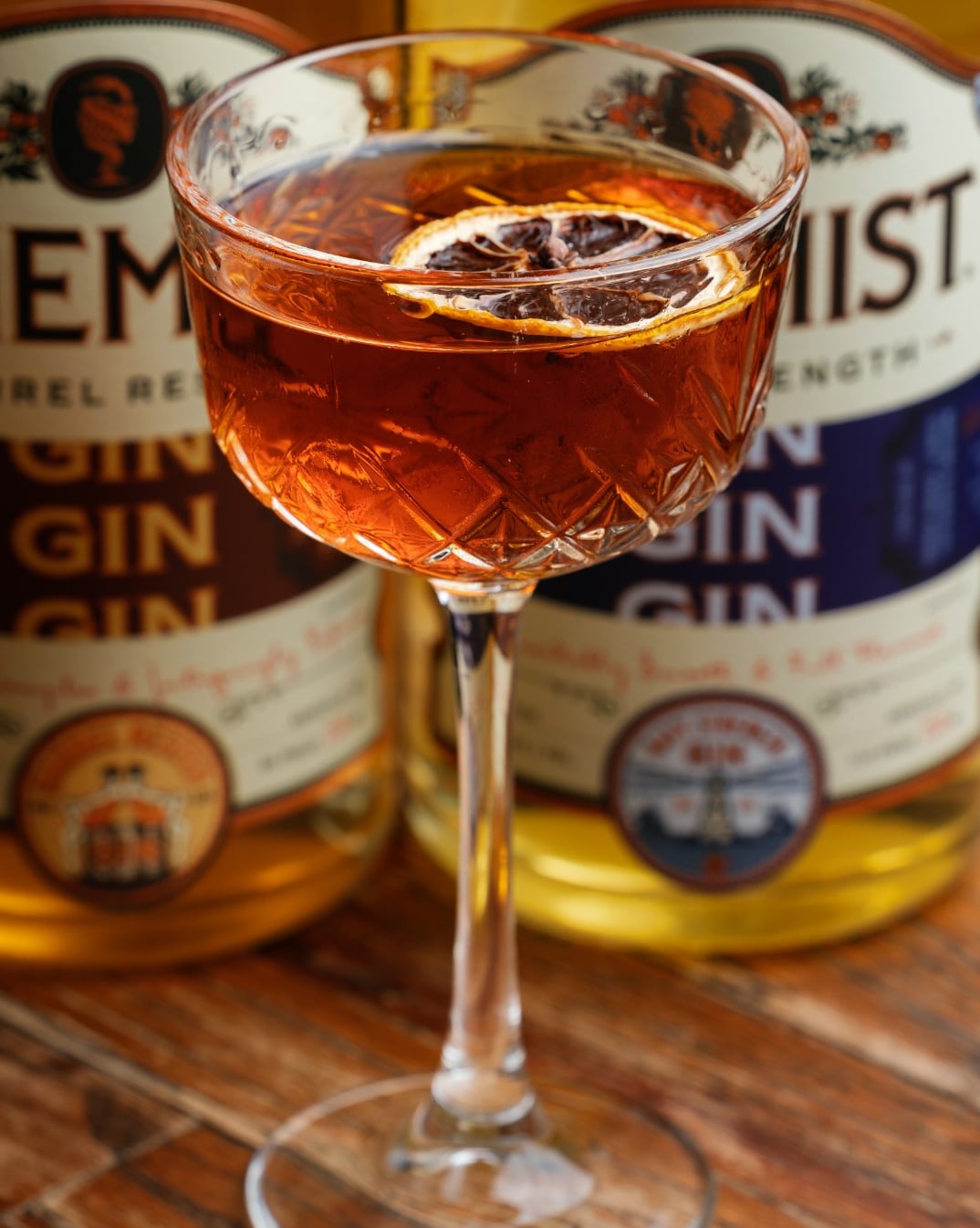 Amber cocktail served in a coupe glass with dried citrus garnish.
