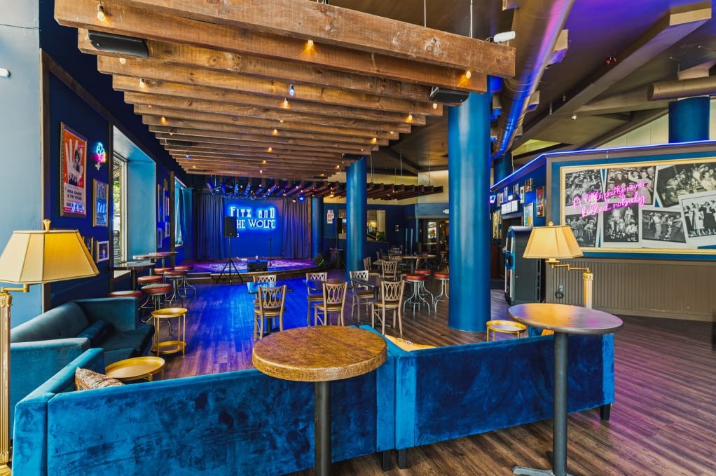 Spacious performance lounge with rustic wooden ceiling beams and deep blue velvet seating.