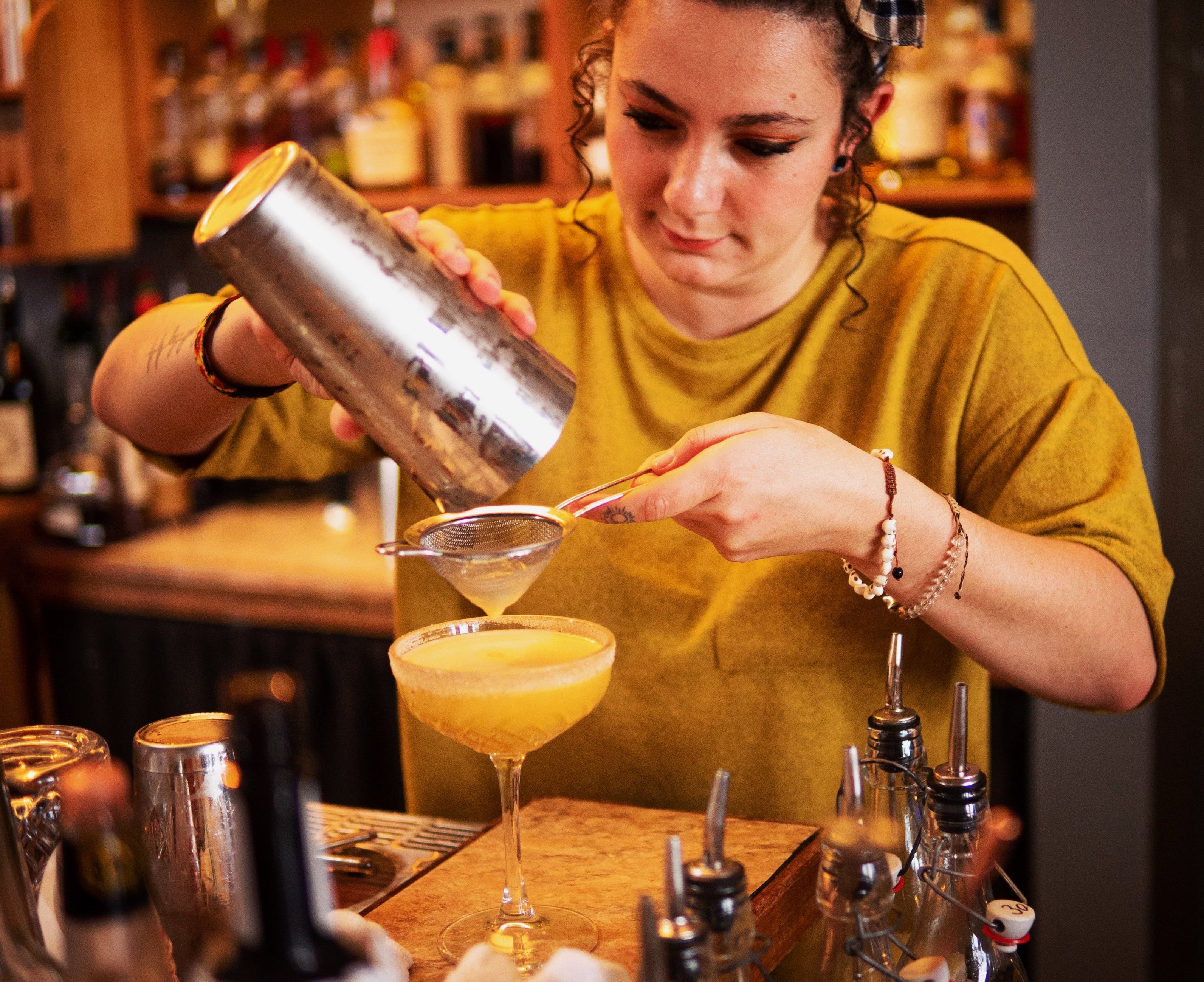 Bartender at work behind the bar, straining a coupe