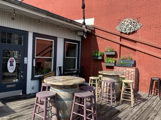 Rooftop patio with barrel tables, pink stools, string lights, and exposed brick walls