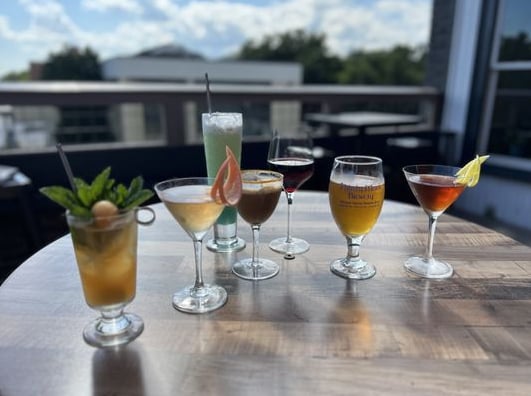 Variety of handcrafted cocktails on the rooftop patio with Asheville skyline in the background