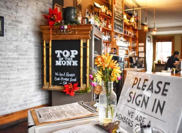 Top of the Monk bar interior with chalkboard sign, exposed brick wall, and backbar spirits
