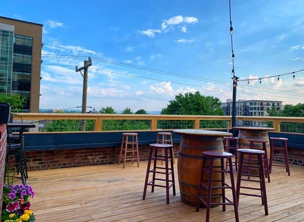 Rooftop patio with barrel tables, string lights, and Blue Ridge Mountain views