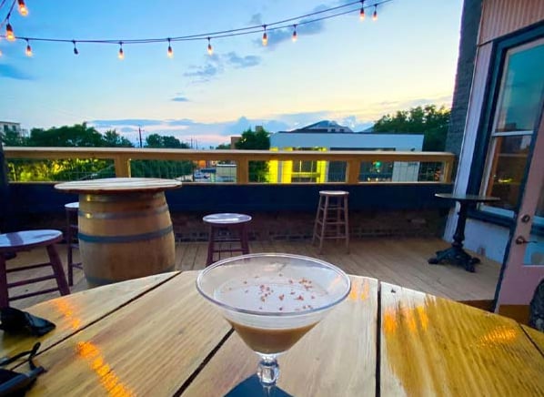 Craft cocktail on the rooftop patio at sunset with mountain views and string lights