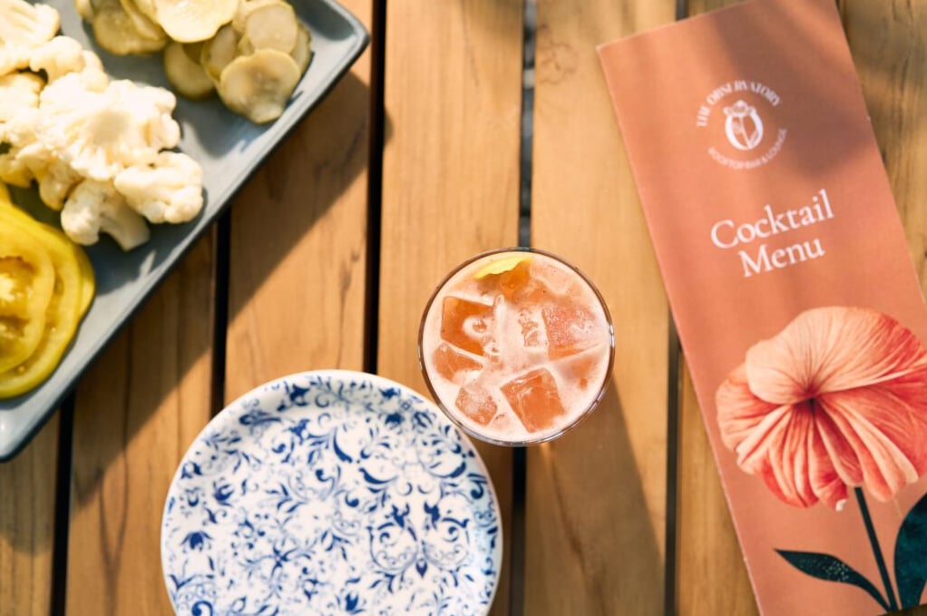 Pink cocktail served with appetizers on a reclaimed wood table