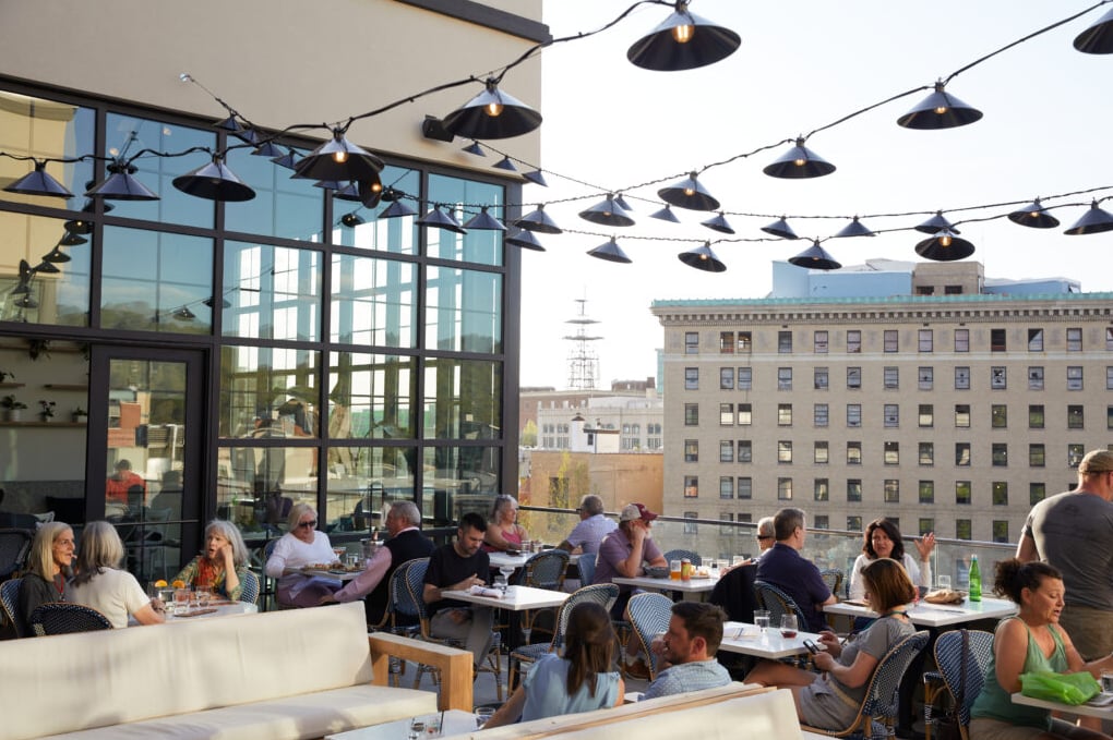 Bustling sunlit rooftop patio with string lighting and urban skyline views