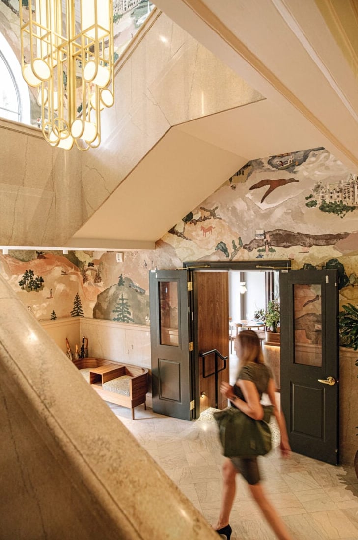 Hotel lobby with hand-painted mountain mural, marble staircase, and art deco chandelier
