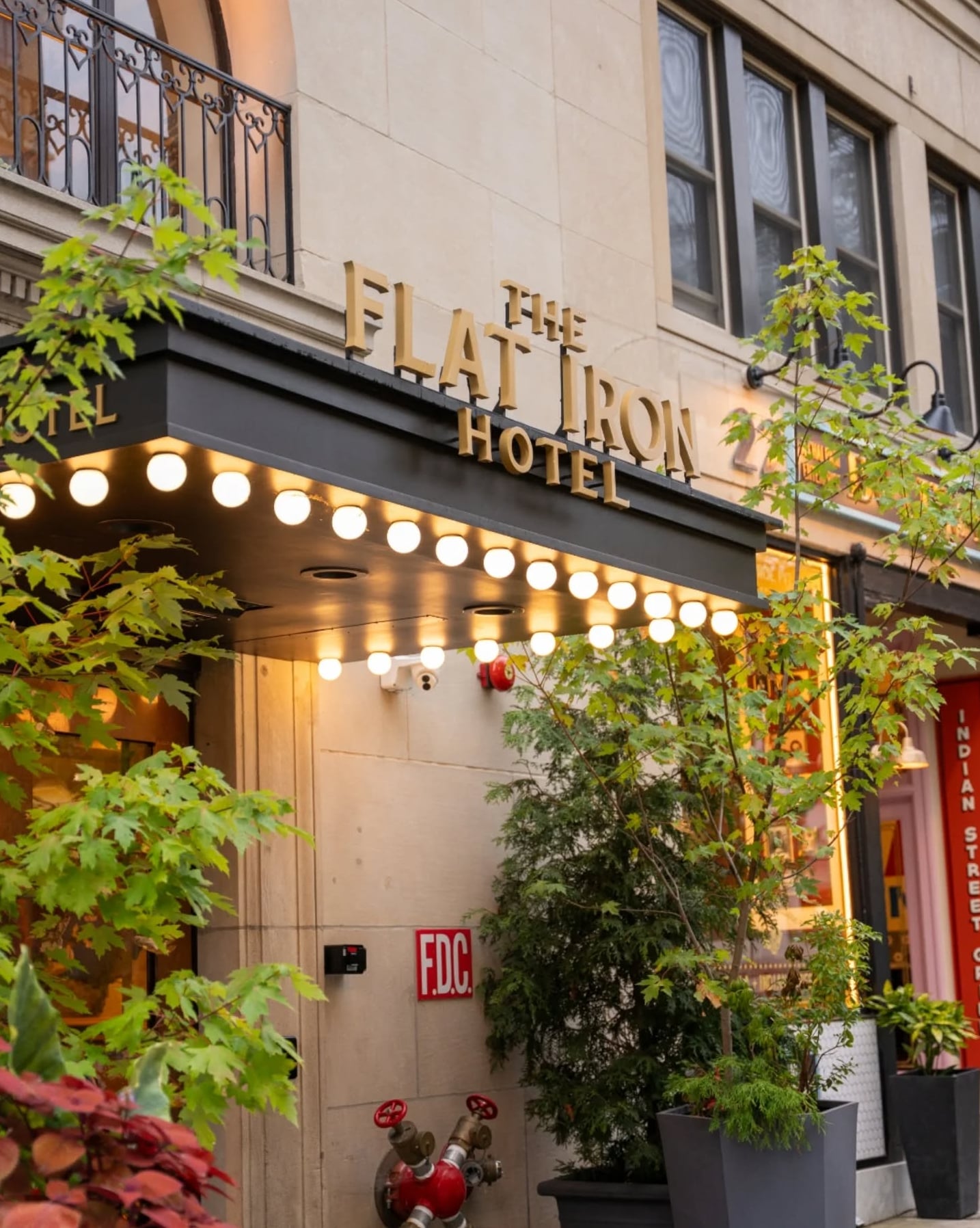 The Flat Iron Hotel exterior entrance with illuminated marquee and greenery