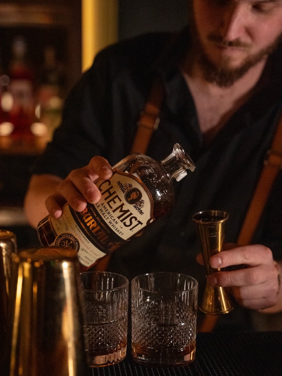 Expert bartender pouring premium whiskey into crystal rocks glasses