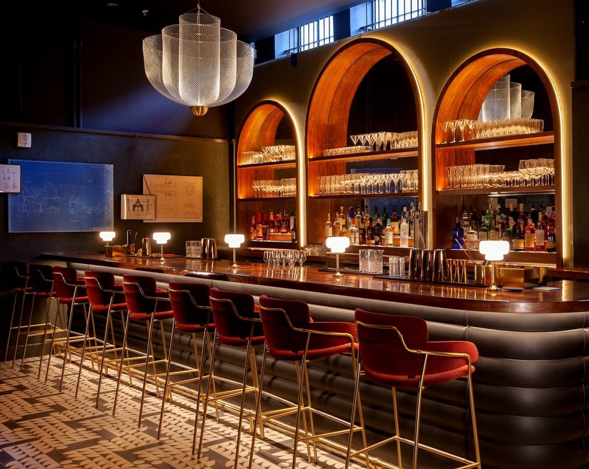 Elegant bar interior with arched shelving, ambient lighting, and plush red seating.