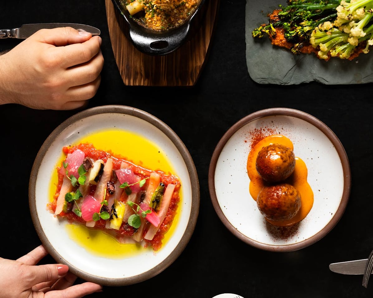 Summer tapas flatlay featuring crudo, meatballs, and charred broccolini