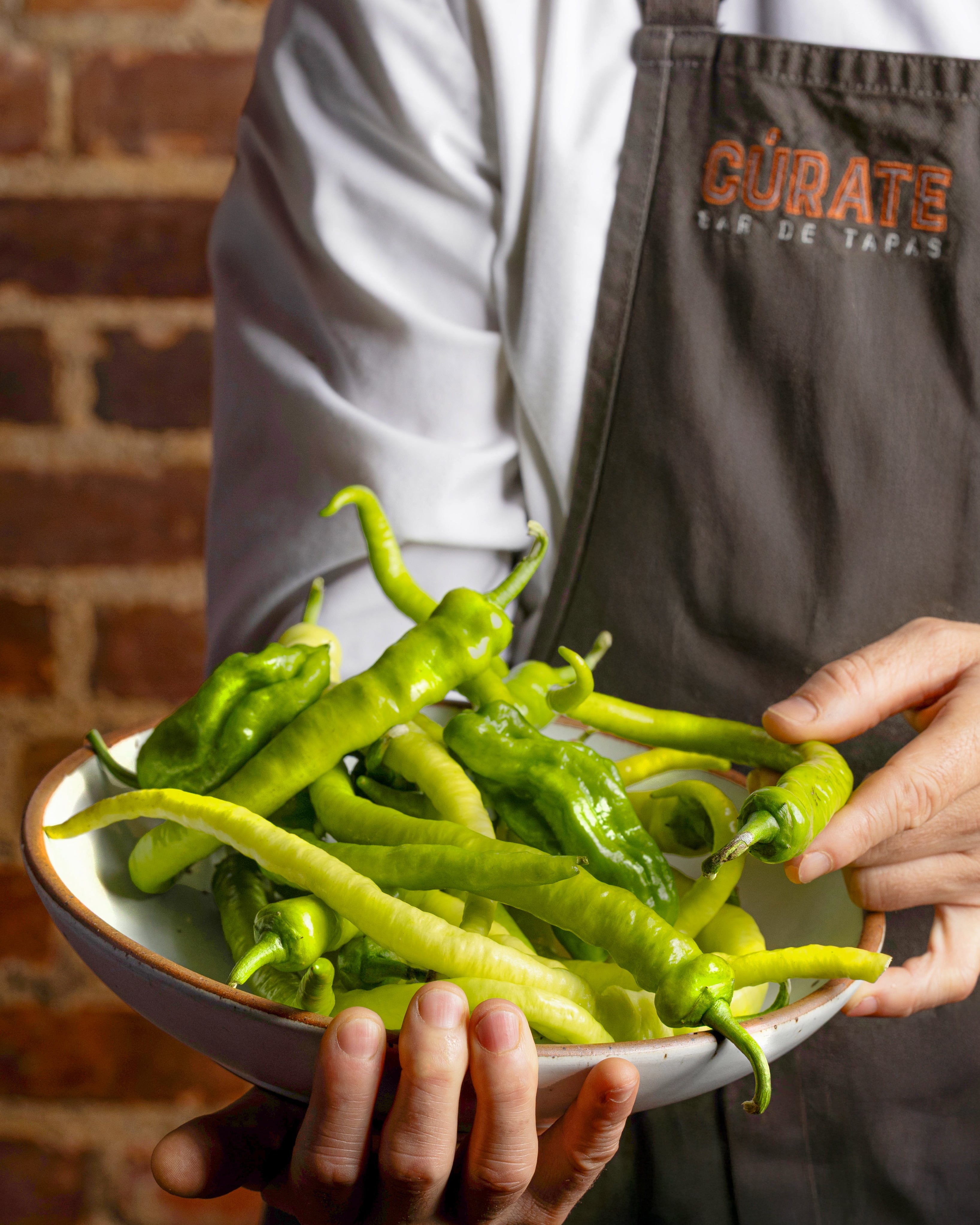 Server in Cúrate Bar de Tapas attire presenting roasted Padrón peppers