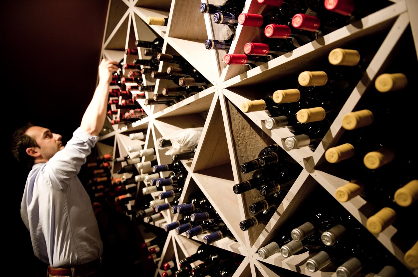 Guest selecting from an extensive collection stored in modern geometric wine racks.