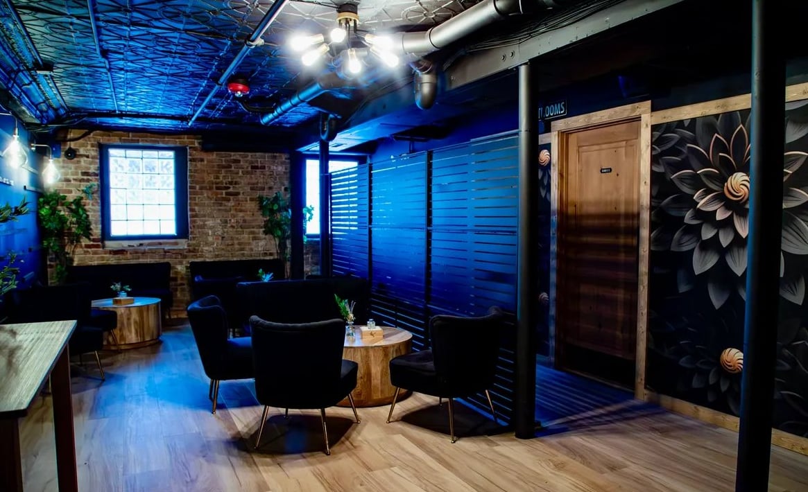 Intimate lounge seating area with blue accent lighting, exposed brick, and floral mural