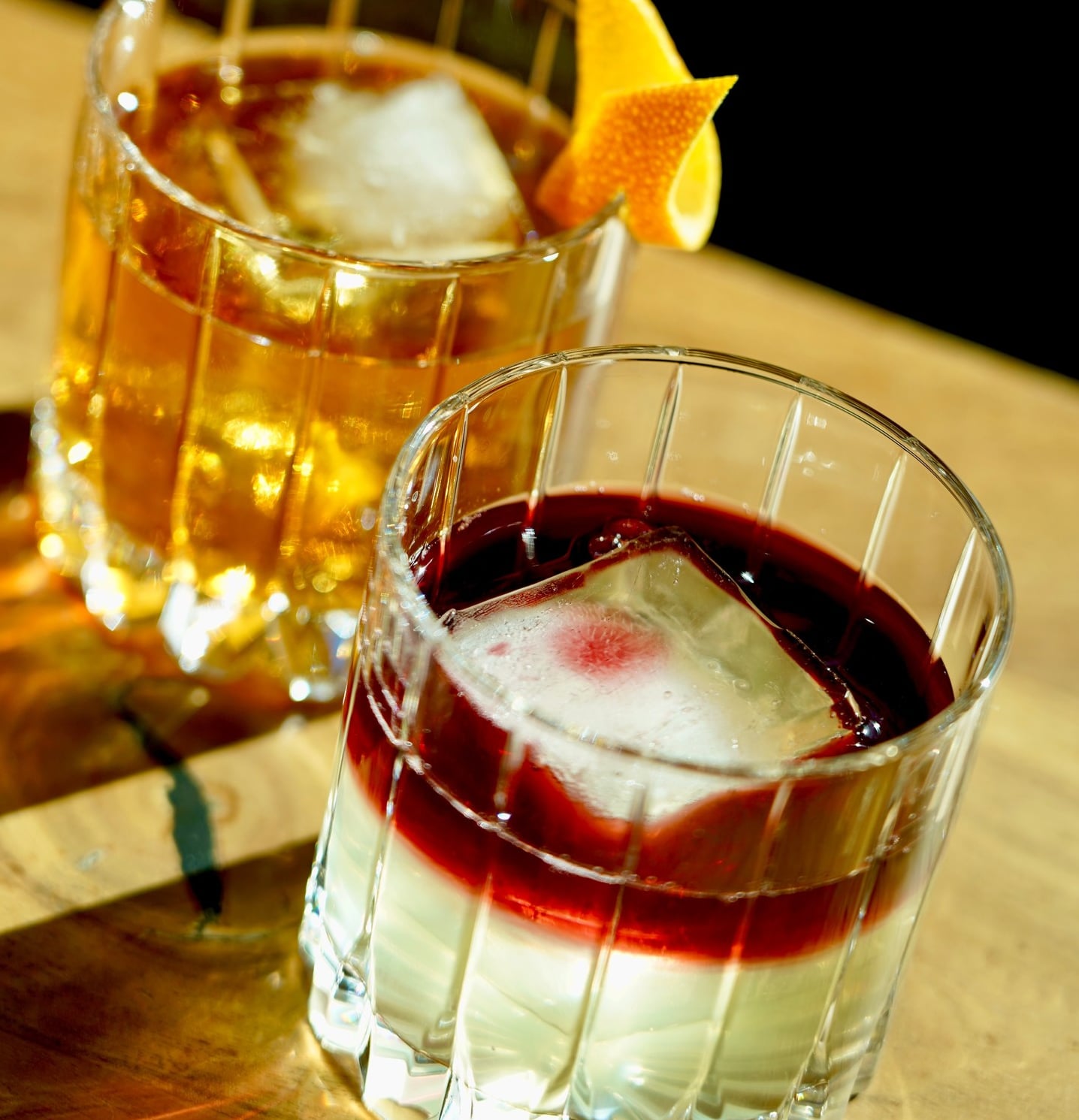 Artisanal layered cocktail served with a large clear ice cube.