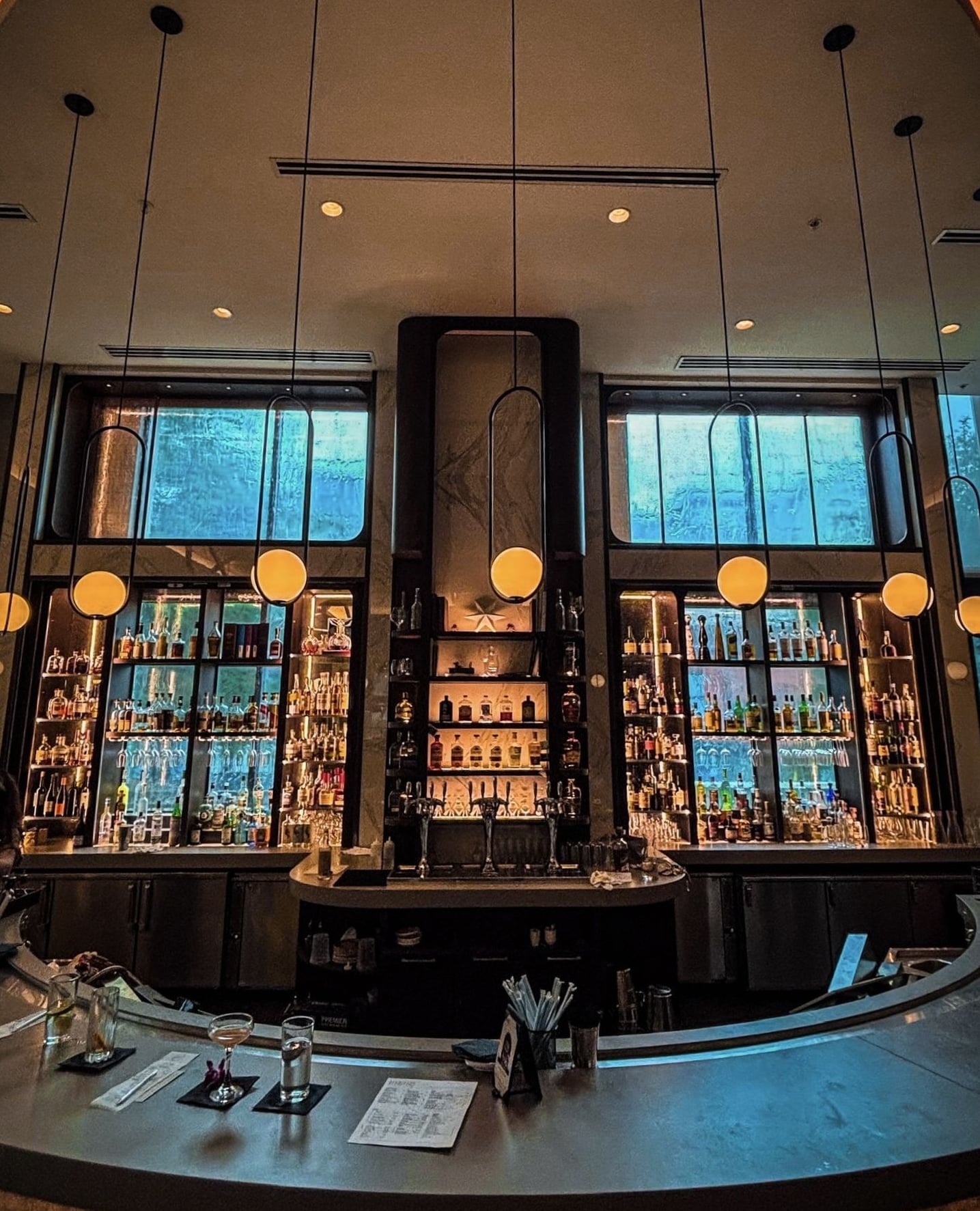 Modern curved bar featuring warm pendant lighting and an extensive display of spirits.