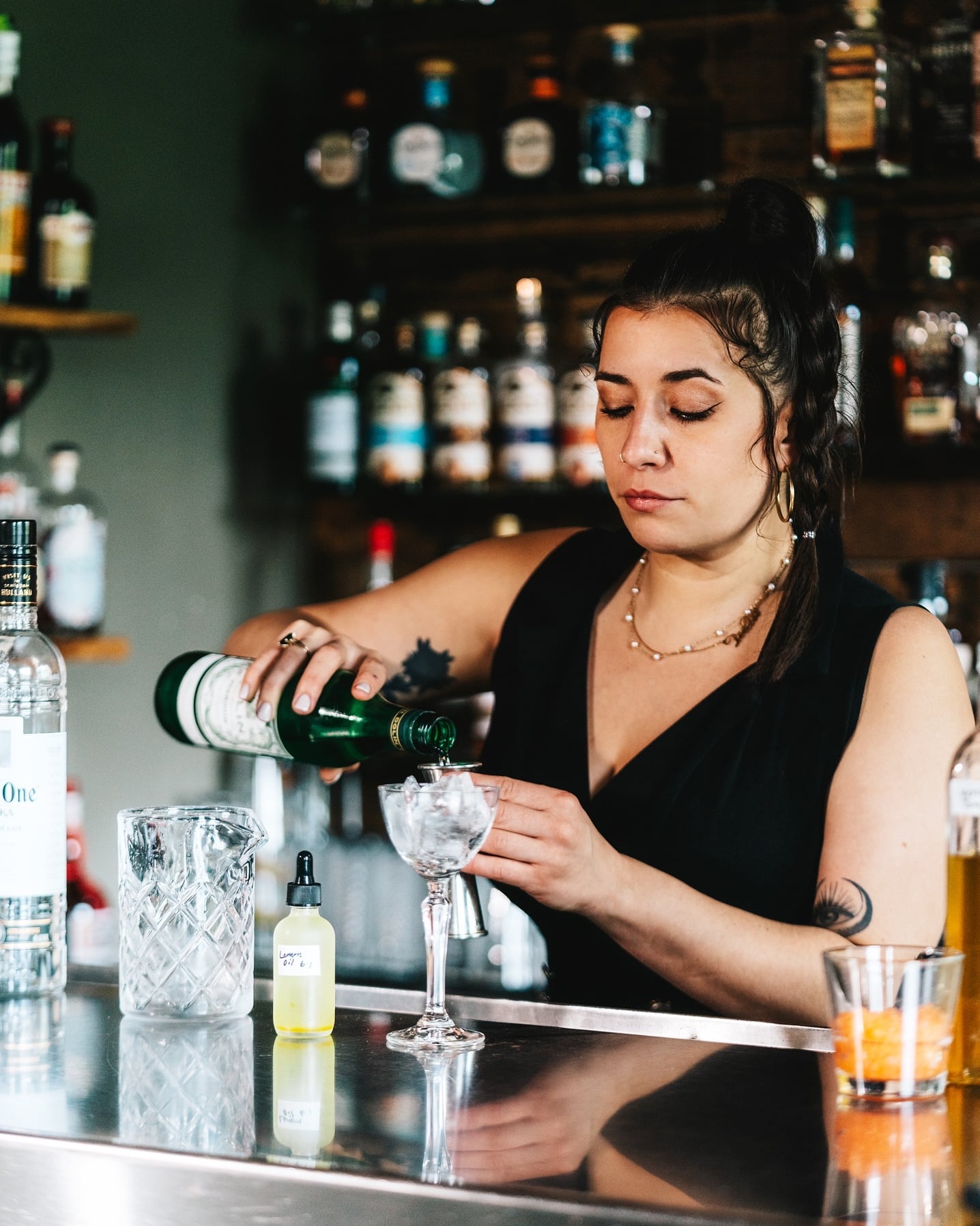 Bartender crafting cocktails at the bar with full shelves of spirits.