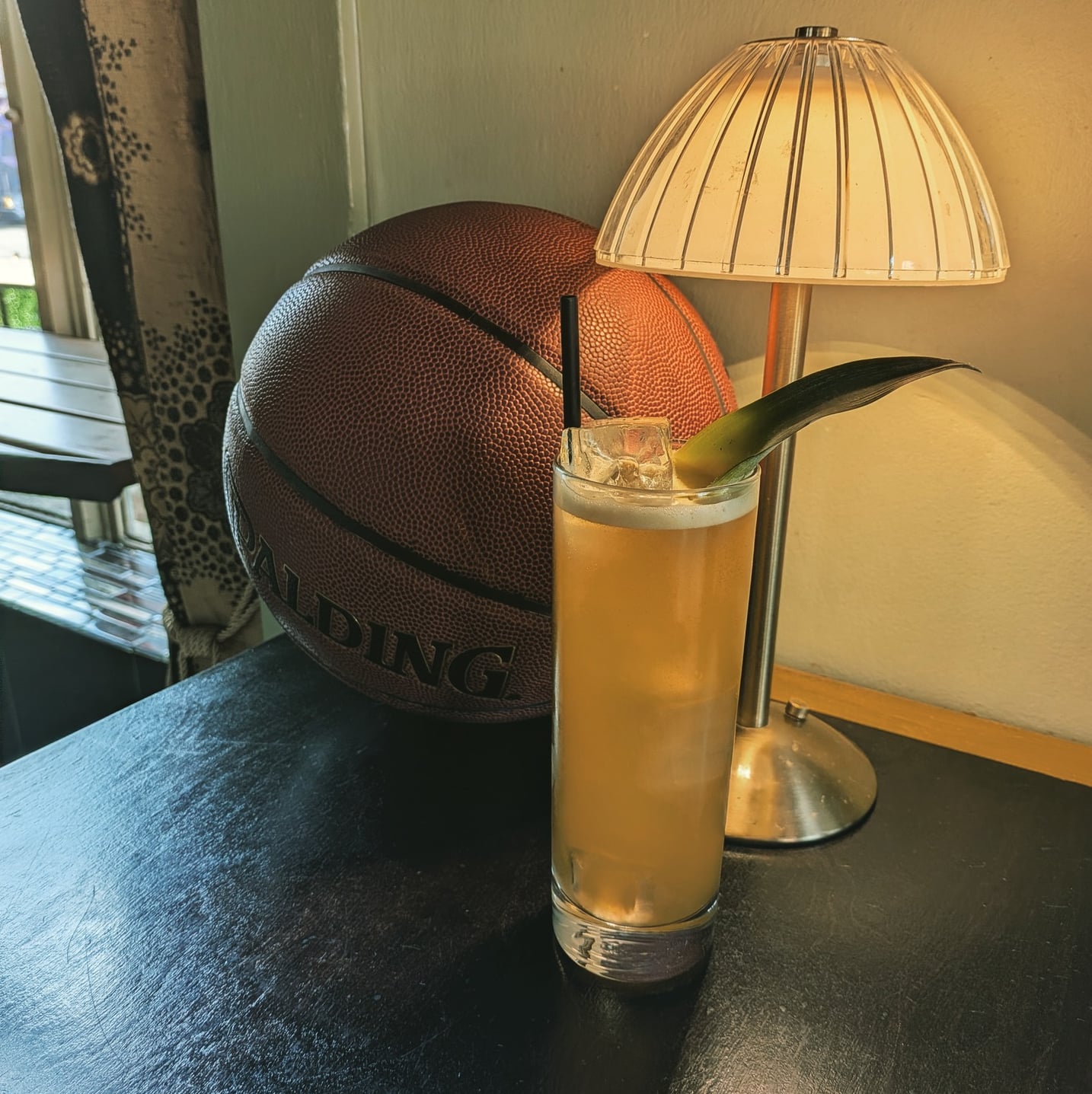 Long cocktail with citrus garnish paired with quirky decor featuring a basketball and vintage-style lamp.