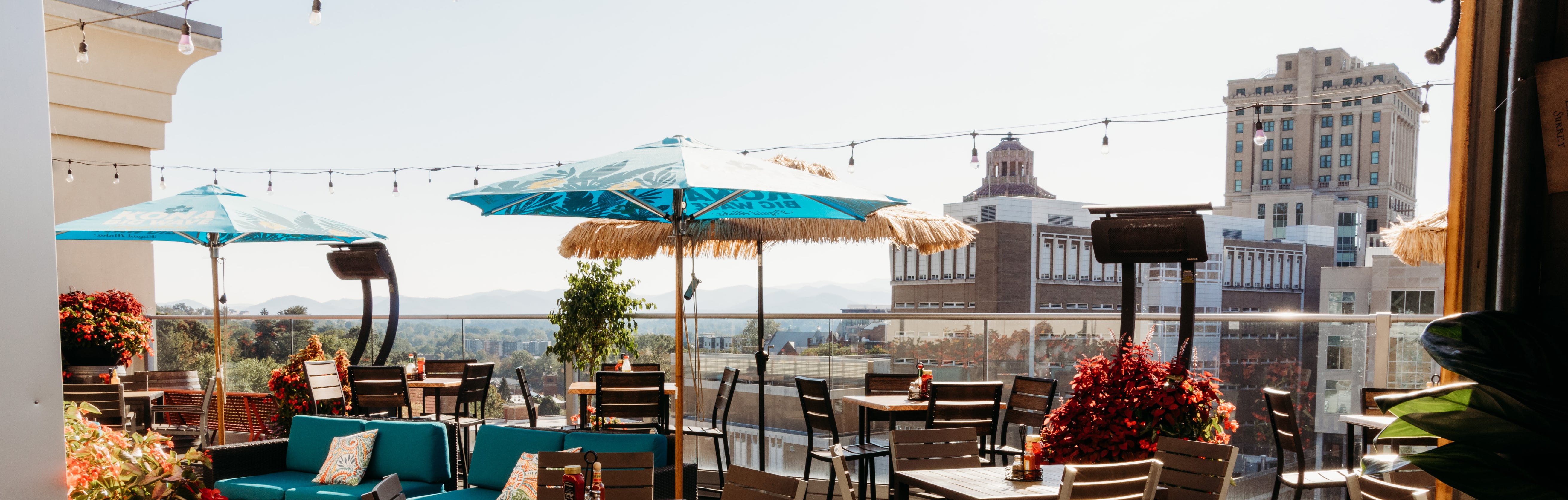 Rooftop terrace at Pillar with colorful umbrellas, string lights, and panoramic views of the Asheville skyline and Blue Ridge Mountains