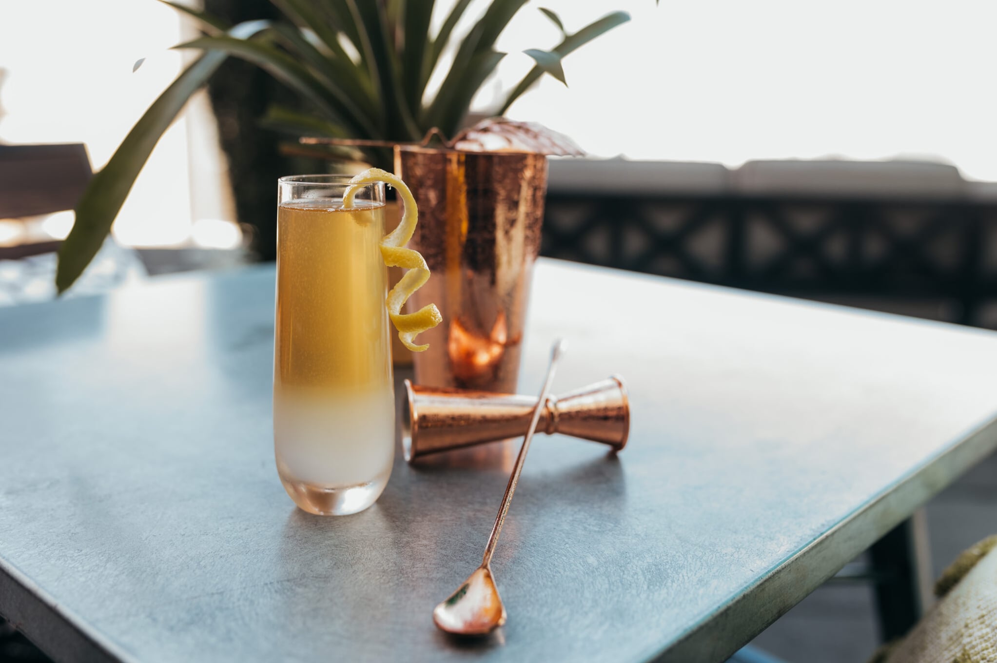 Citrus collins cocktail with lemon twist and copper shaker on the rooftop terrace