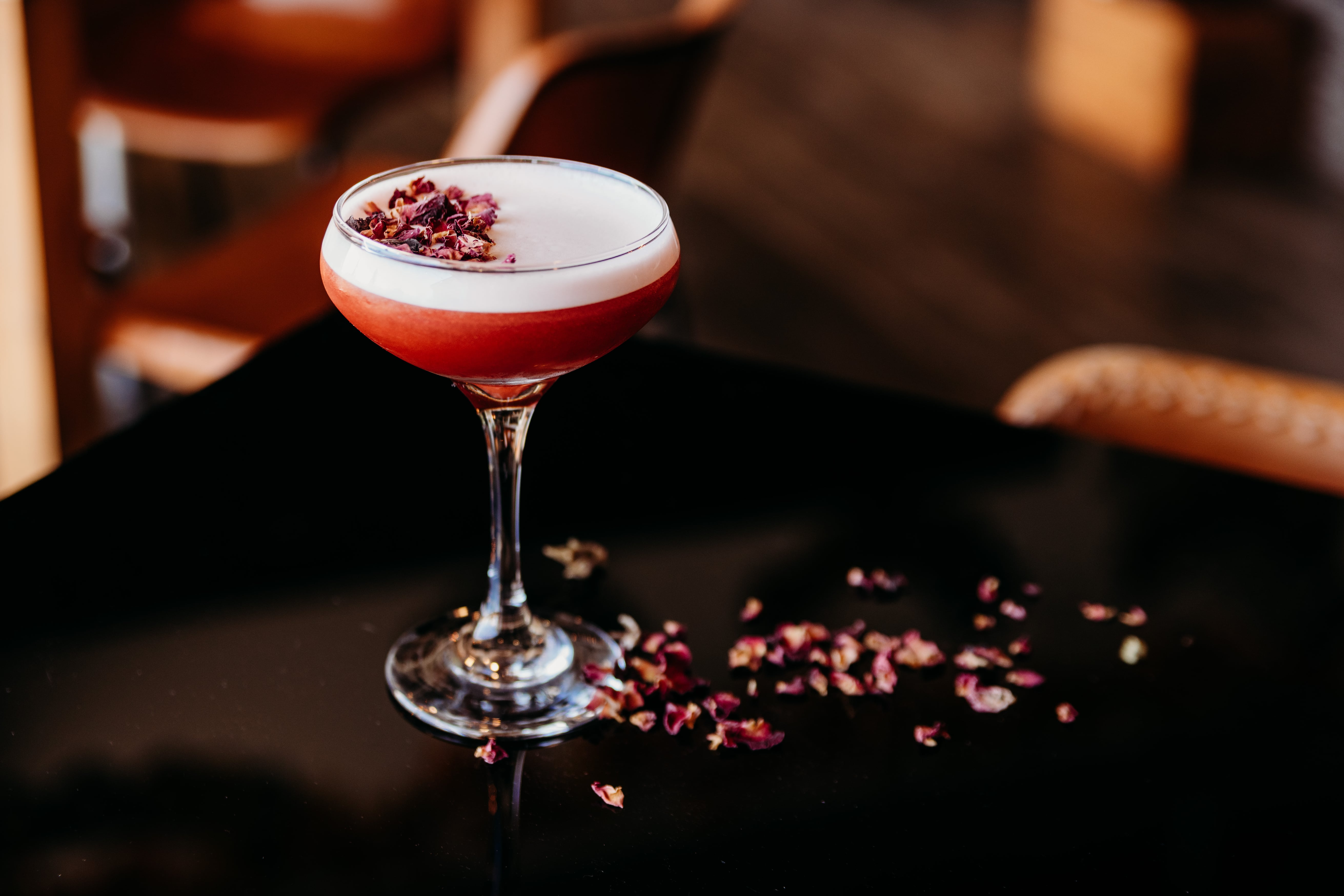 Crimson coupe cocktail with dried rose petal garnish, served at the dark marble bar