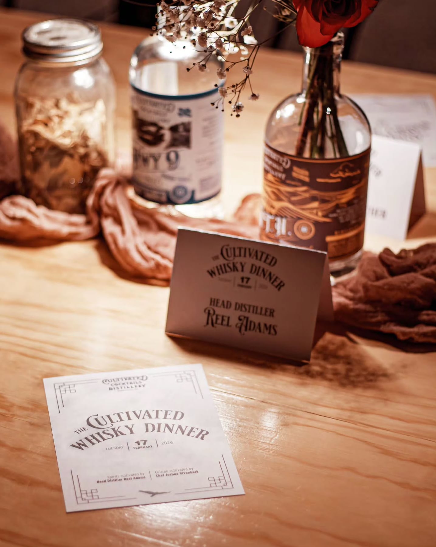 Event detail shot: The Cultivated Whisky Dinner table setup featuring custom branding and floral accents.