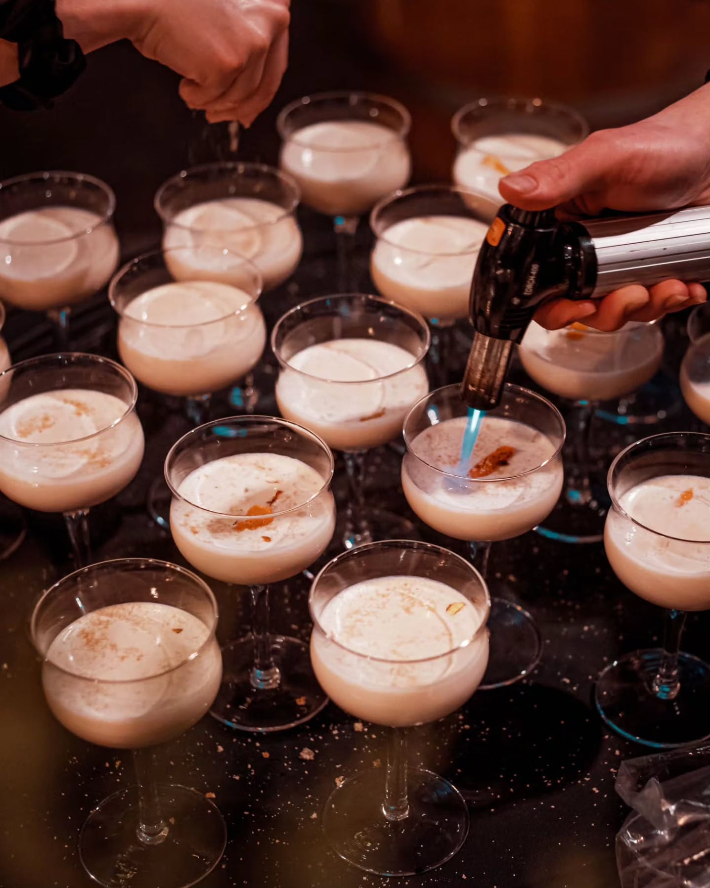 Bartenders using torches to finish cream-based cocktails in coupe glasses.